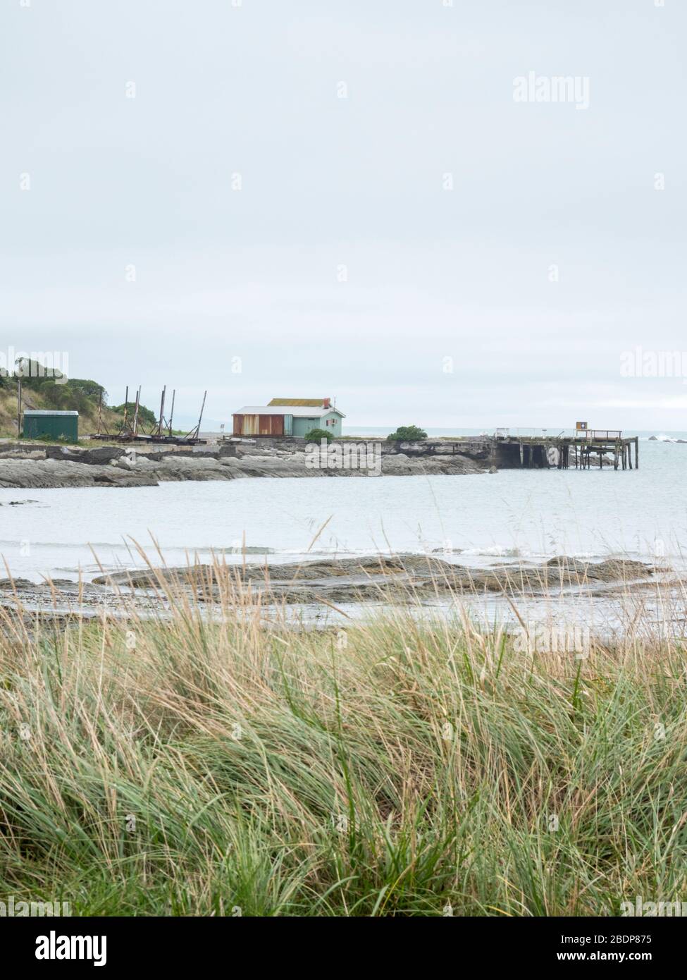 Un vecchio porto di pesca e molo nel paesaggio sulla costa rocciosa e sulla costa e a Point Kean Kaikoura Nuova Zelanda in un giorno grigio. Foto Stock