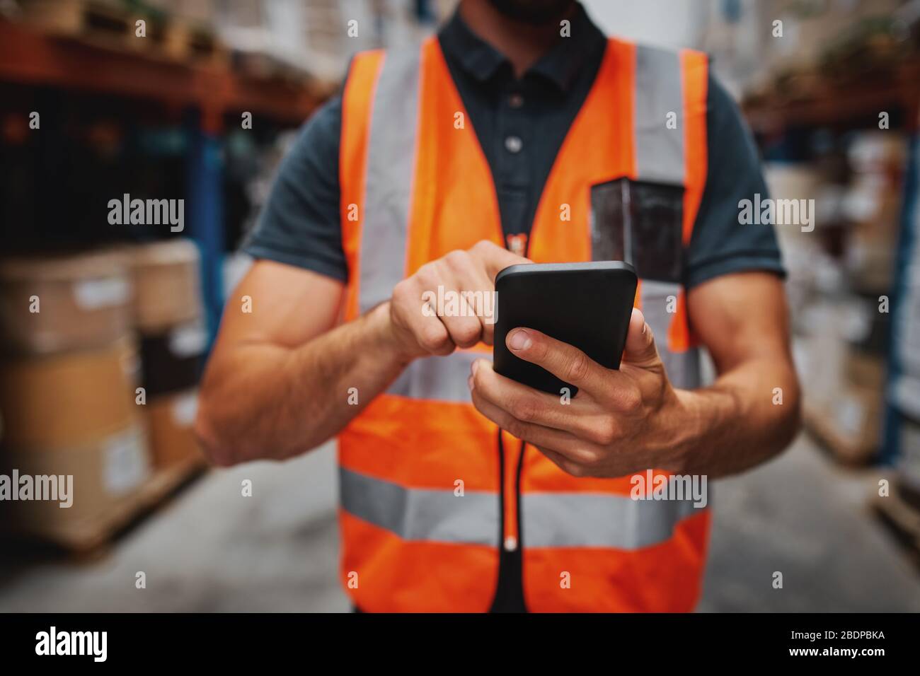 Primo piano delle mani dell'uomo con il telefono cellulare mentre in magazzino in uniforme Foto Stock