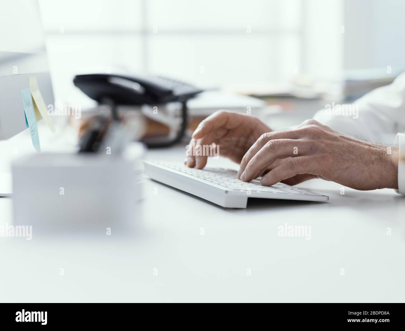 Uomo d'affari che lavora con il suo computer in ufficio, sta digitando sulla tastiera, mani vicine Foto Stock