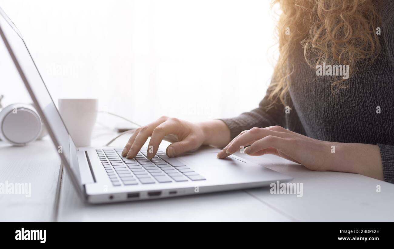 Donna seduta alla scrivania e in collegamento con il suo computer portatile, sta lavorando e digitando sulla tastiera, le mani si avvicinano Foto Stock