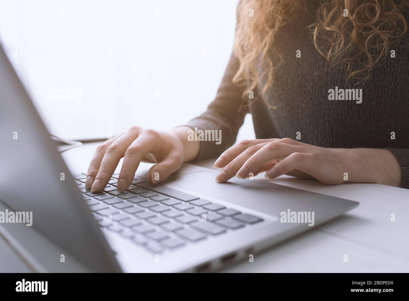 Donna seduta alla scrivania e in collegamento con il suo computer portatile, sta lavorando e digitando sulla tastiera, le mani si avvicinano Foto Stock