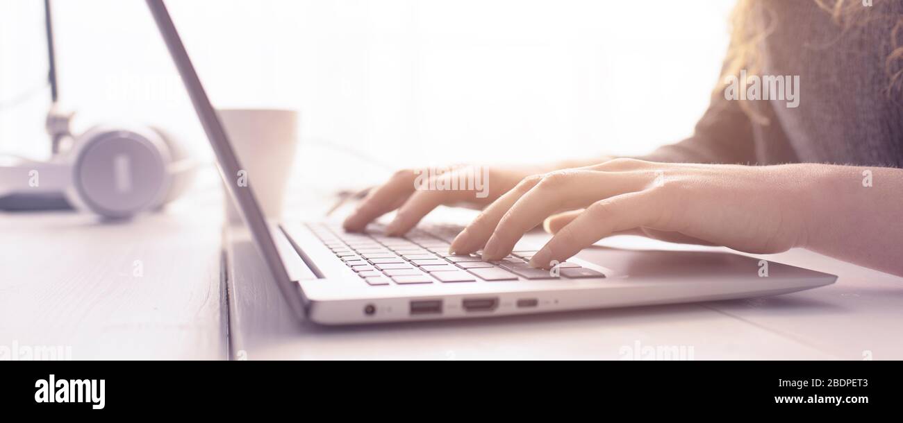 Donna seduta alla scrivania e in collegamento con il suo computer portatile, sta lavorando e digitando sulla tastiera, le mani si avvicinano Foto Stock