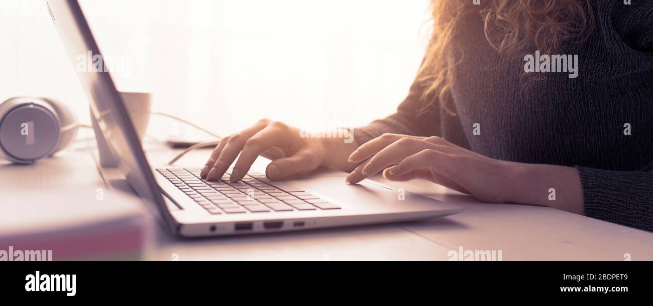 Donna seduta alla scrivania e in collegamento con il suo computer portatile, sta lavorando e digitando sulla tastiera, le mani si avvicinano Foto Stock