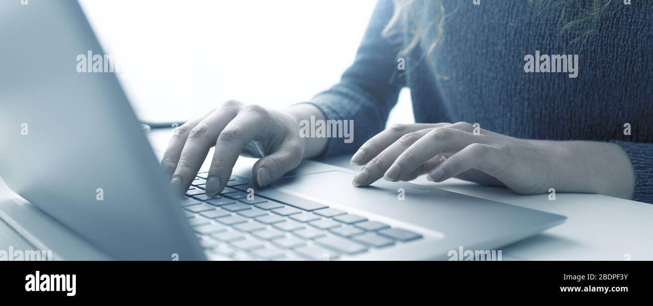 Donna seduta alla scrivania e in collegamento con il suo computer portatile, sta lavorando e digitando sulla tastiera, le mani si avvicinano Foto Stock