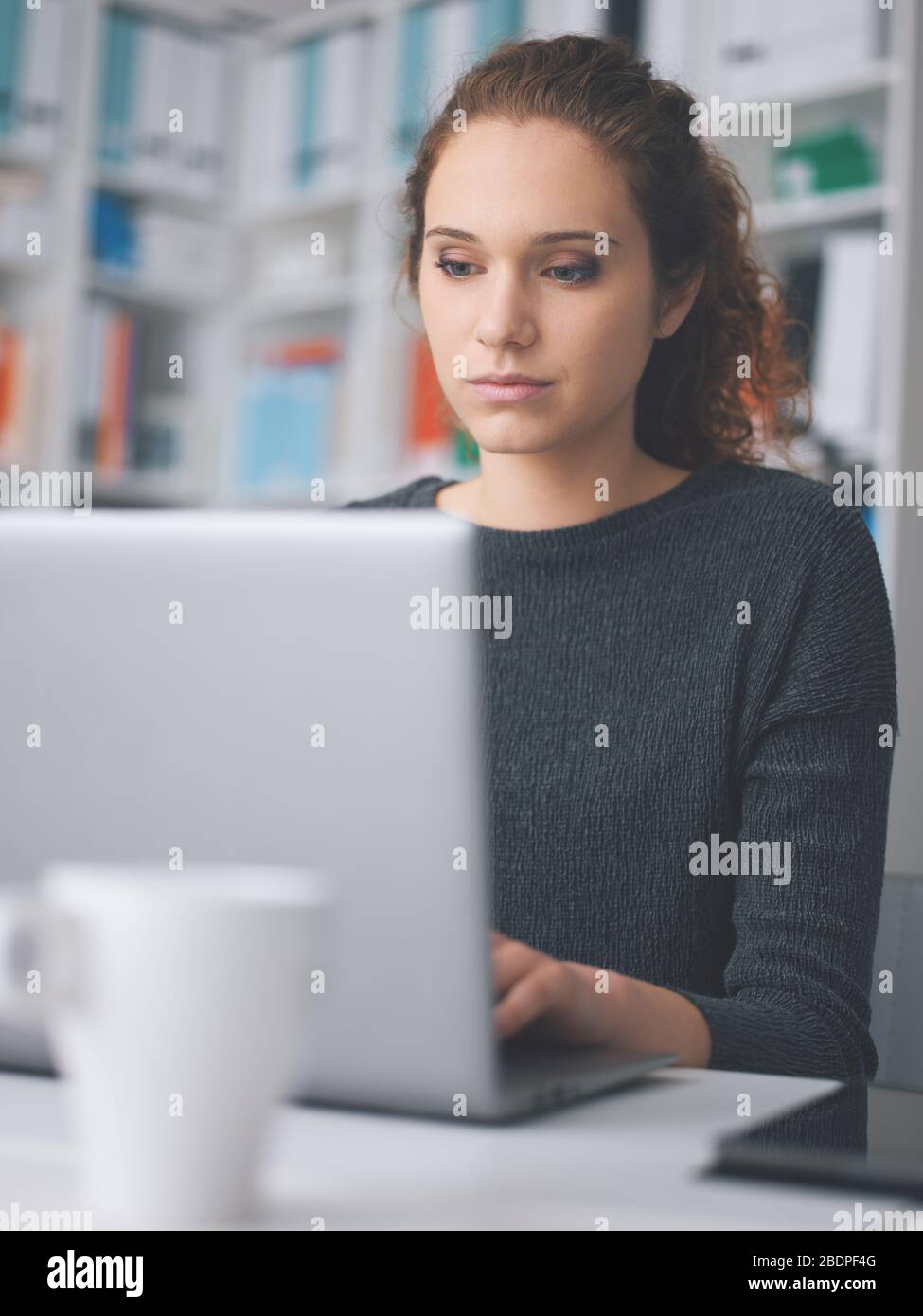 Giovane donna seduto alla scrivania in ufficio e che lavora con un computer portatile Foto Stock