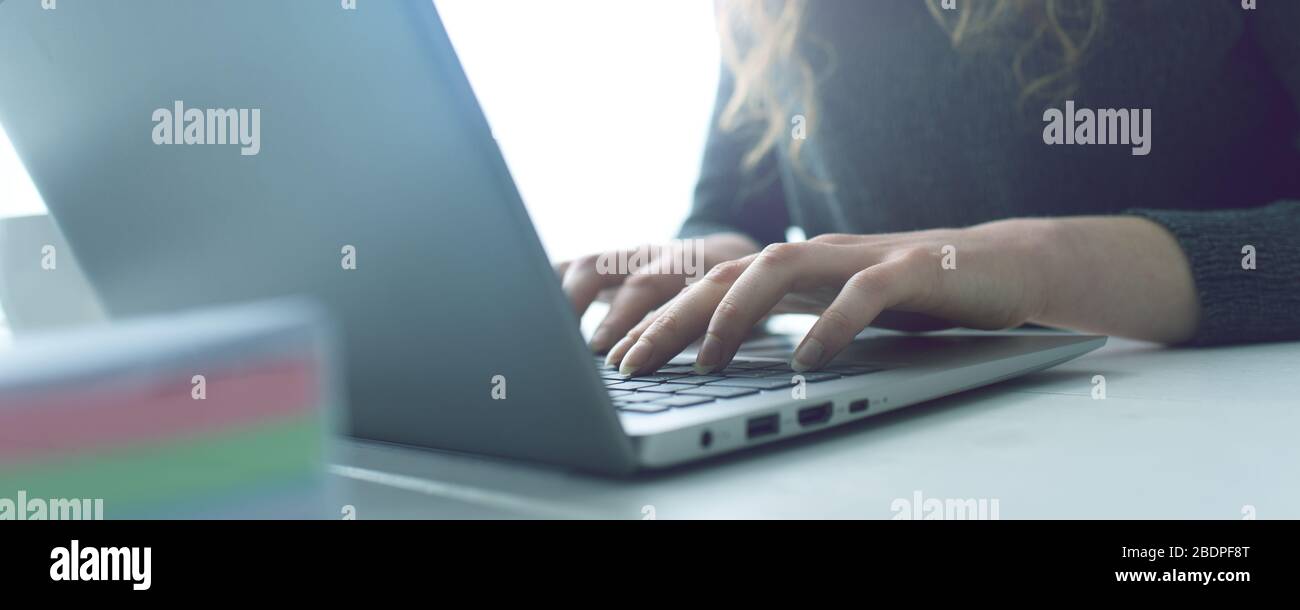 Donna seduta alla scrivania e in collegamento con il suo computer portatile, sta lavorando e digitando sulla tastiera, le mani si avvicinano Foto Stock