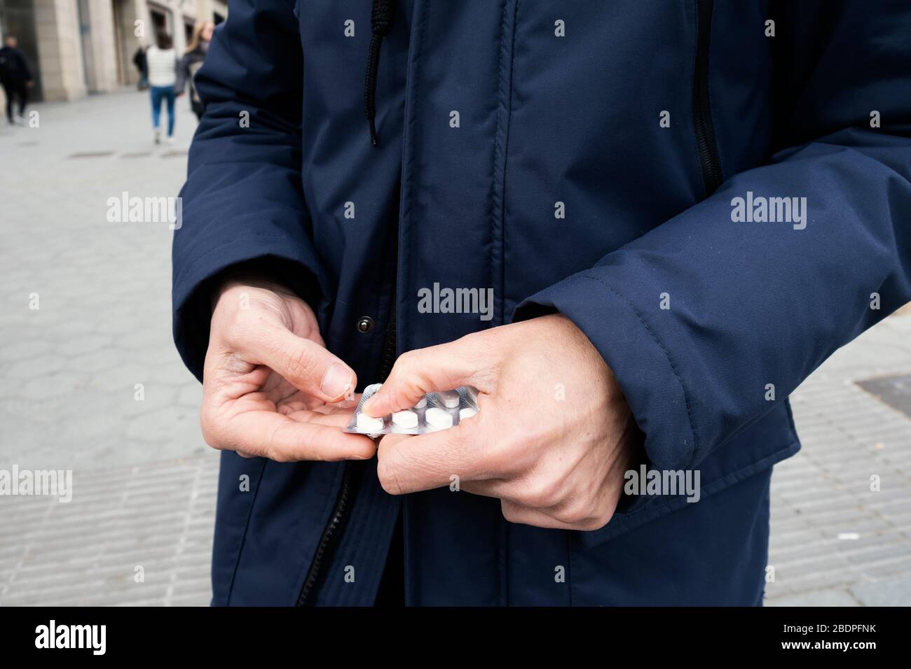 primo piano di un uomo caucasico per strada, con un parka blu, ottenendo una pillola da una confezione blister Foto Stock