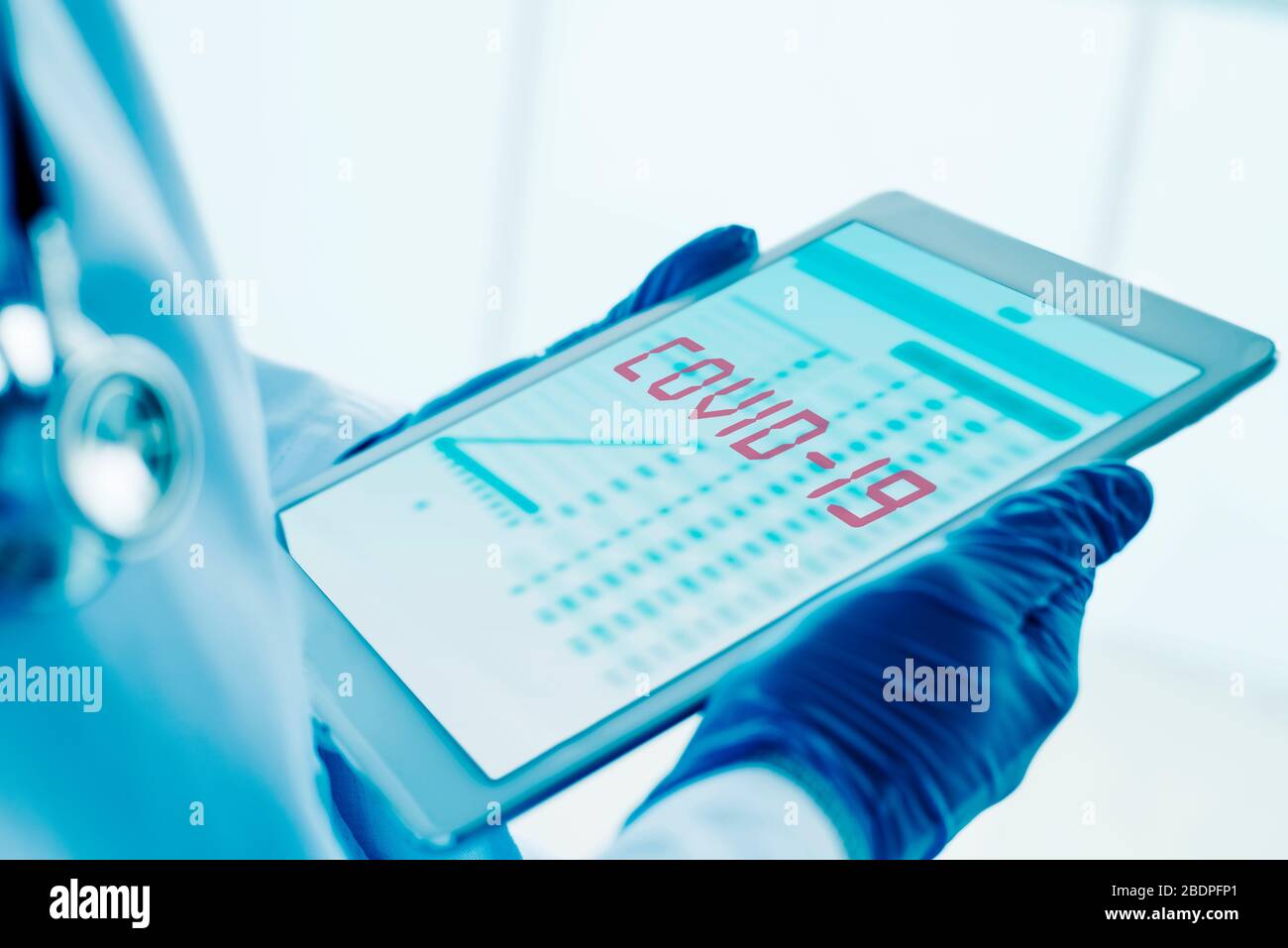 primo piano di un medico, indossando guanti chirurgici blu, avendo una tavoletta digitale nelle sue mani con il testo covid-19 nel suo schermo Foto Stock