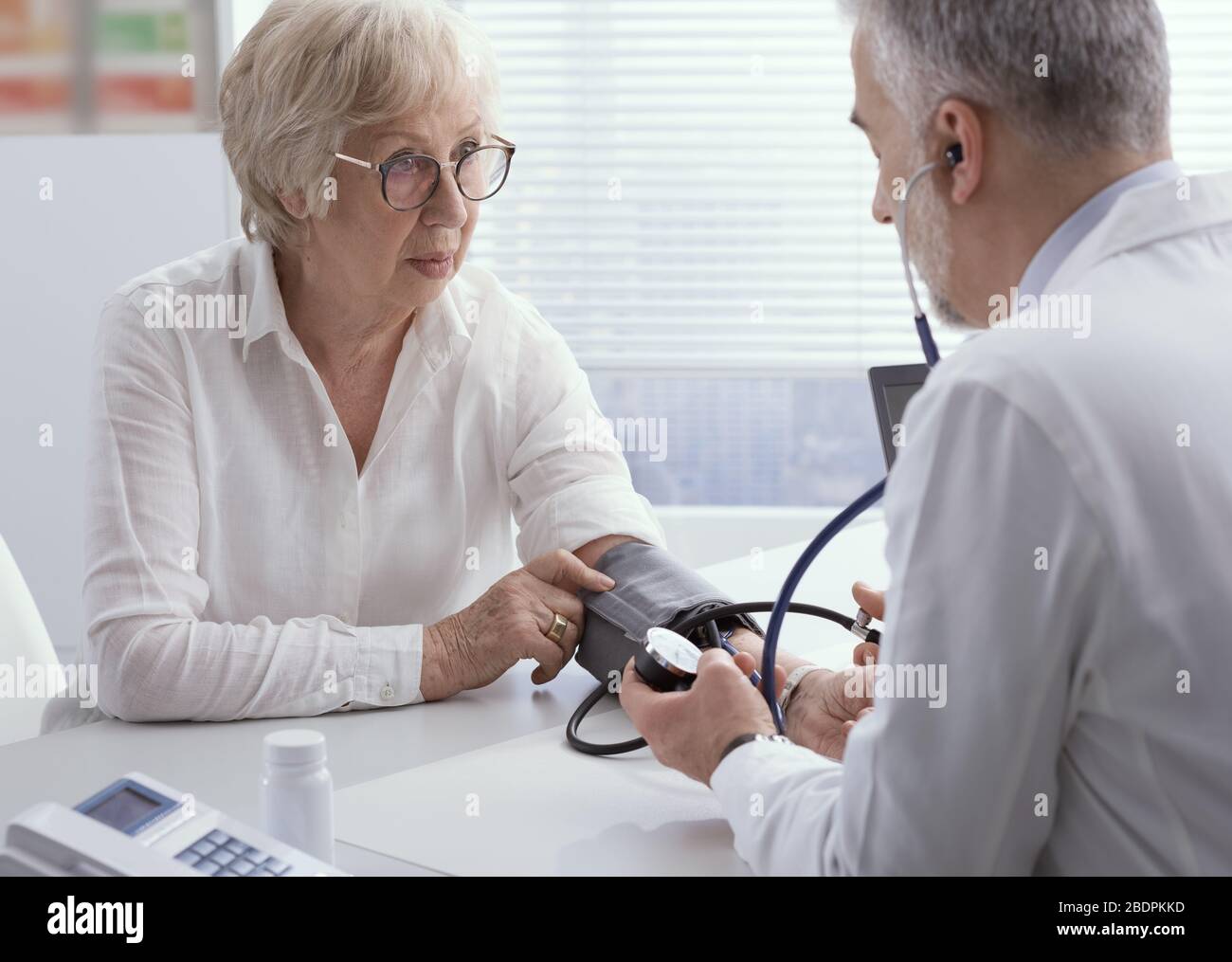 Medico professionista che misura la pressione sanguigna di una paziente di sesso femminile senior durante una visita, ipertensione e prevenzione Foto Stock