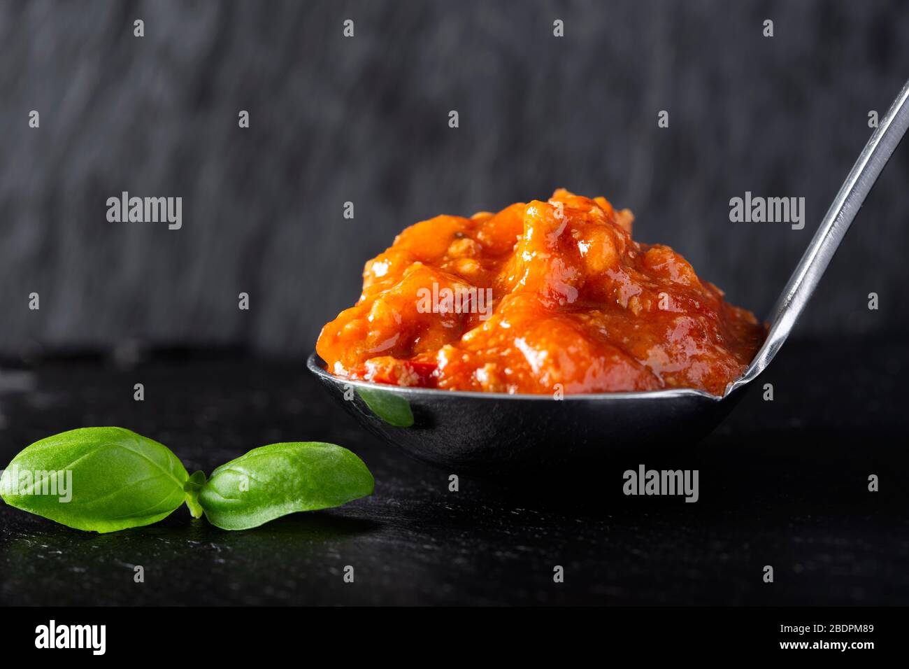 Salsa bolognese italiana in cucchiaio su ardesia scura Foto Stock