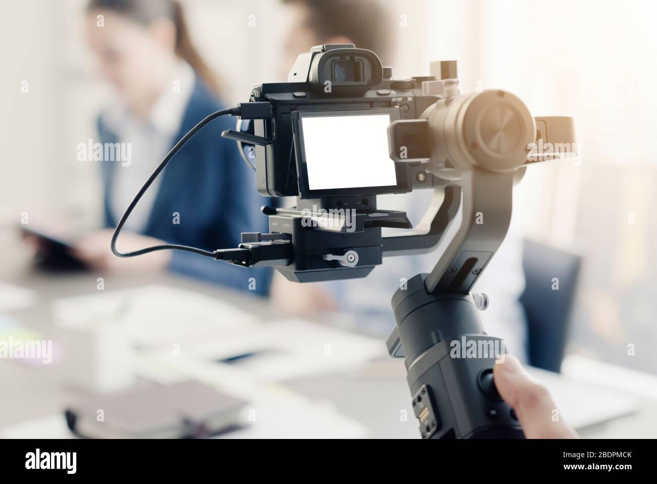 Videomaker professionale che scatta un video, attori disfocillati in background, concetto di video e comunicazione Foto Stock