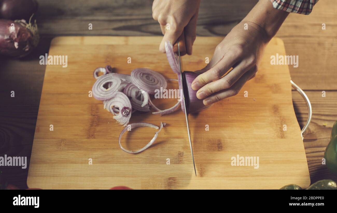 Donna che prepara un pasto vegano sano, sta tagliando le cipolle fresche su un taglio, nutrizione e concetto di stile di vita Foto Stock