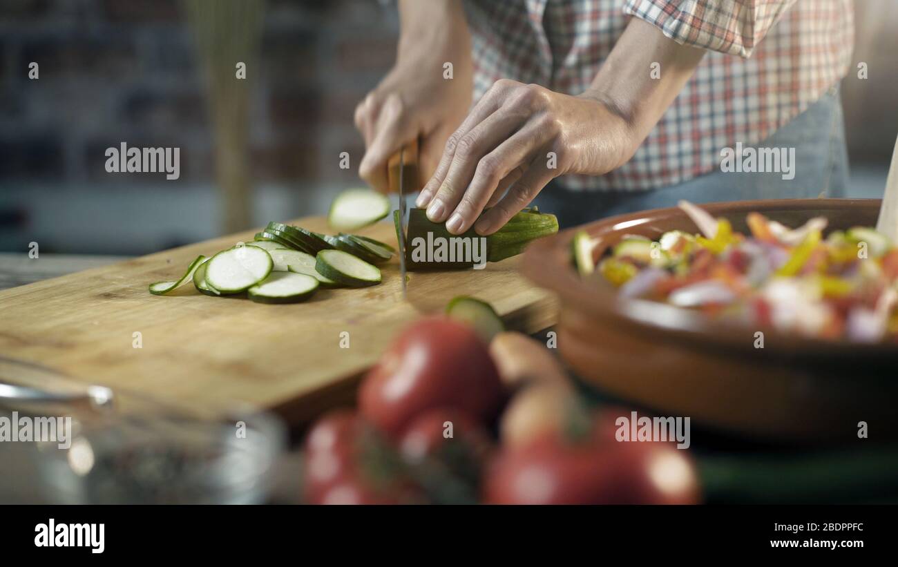 Donna che prepara un sano pasto vegano a casa con verdure fresche, sta tagliando zucchine Foto Stock