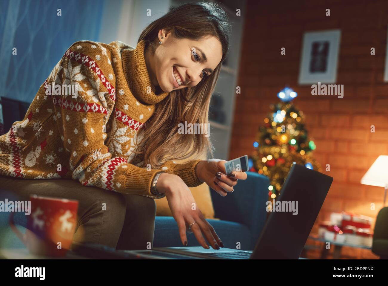 Donna felice che si rilassa sul divano a casa e facendo shopping online, albero di Natale in background Foto Stock