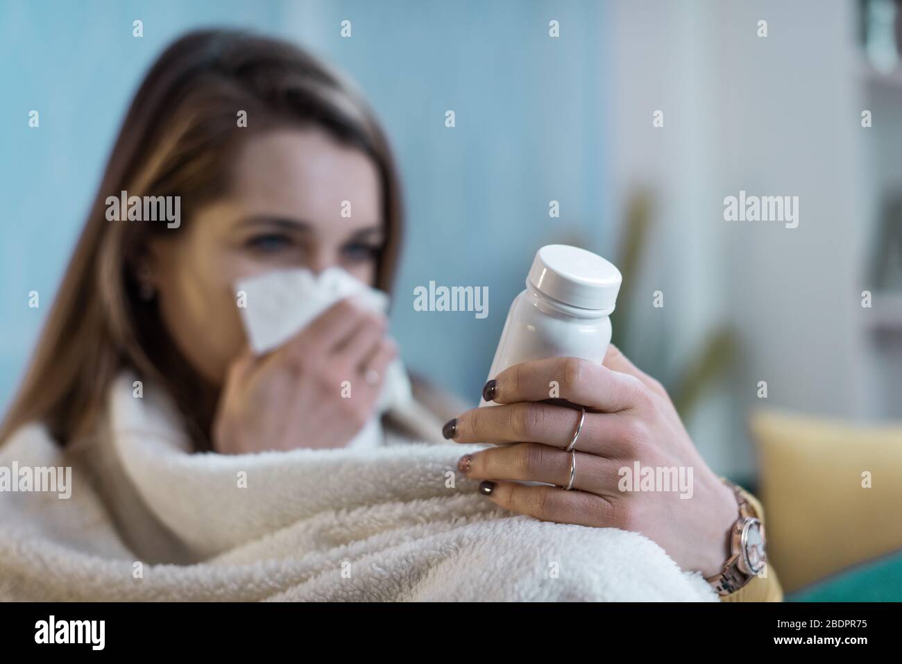 Giovane donna con il freddo e l'influenza, lei sta soffiando il suo naso e le istruzioni di lettura su una bottiglia di medicina di prescrizione Foto Stock