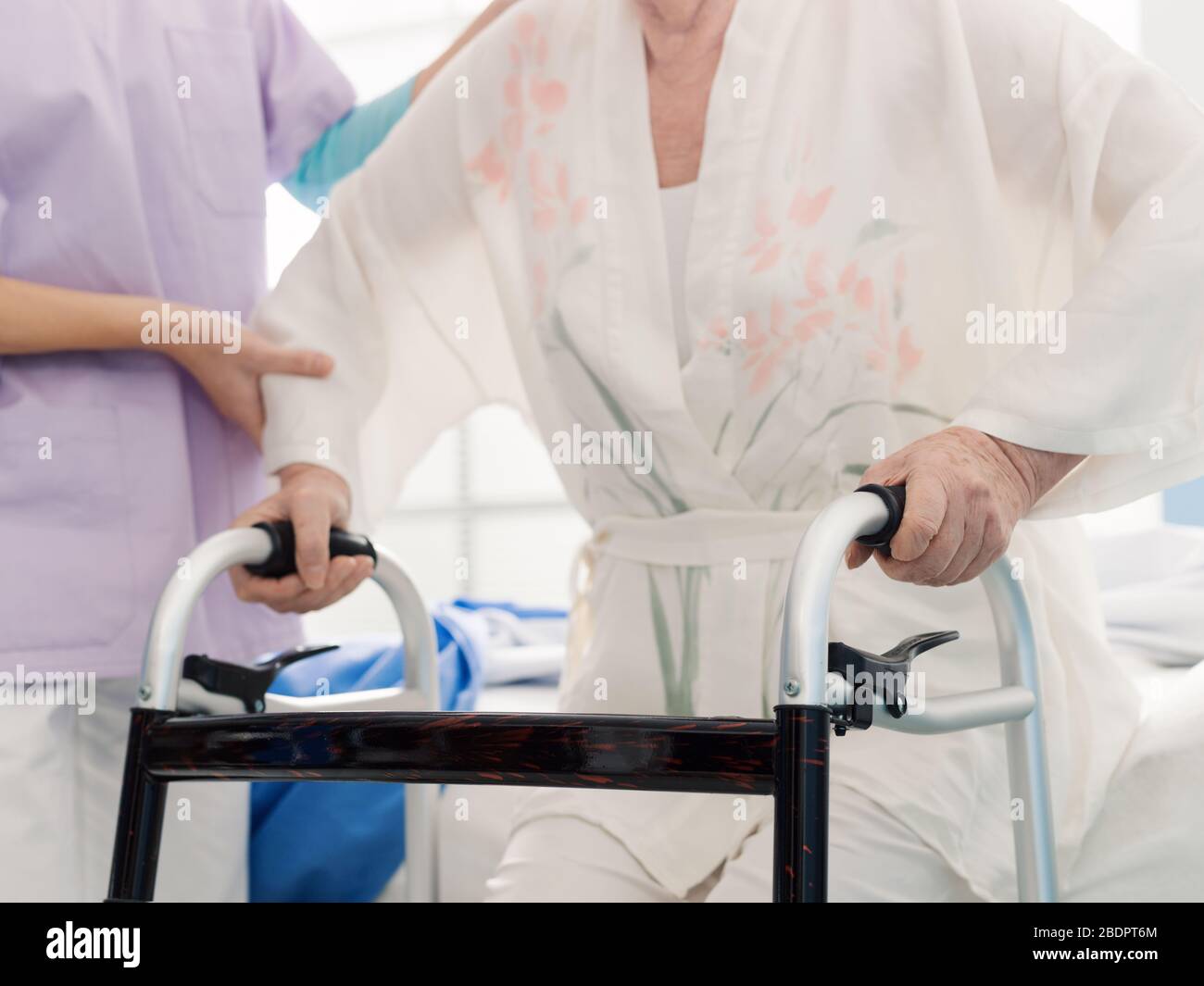 Assistente che assiste una signora anziana alla casa di pensione, la donna sta appoggiando su un camminatore Foto Stock