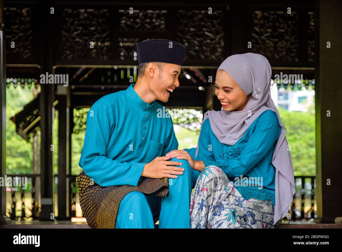 Giovane coppia di musulmani malesi in costume tradizionale che ha una conversazione felice durante la celebrazione di Aidilfitri in casa di legno tradizionale. Raya e Musl Foto Stock