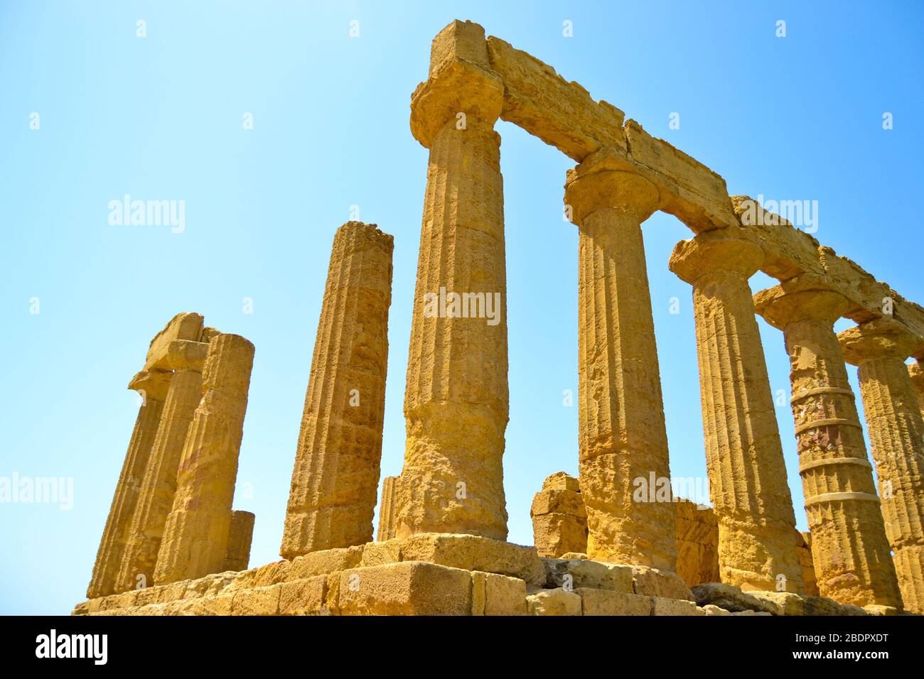 Rovine dorate di un antico tempio greco con colonne rotte e pezzi mancanti sotto un cielo luminoso nell'isola italiana di Sicilia Foto Stock