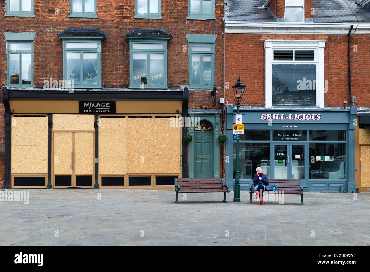Donna solitaria seduta su banco affiancata da negozi e imprese chiusi dopo decreto governativo a seguito dell'epidemia di Corona virus nello Yorkshire, Regno Unito. Foto Stock