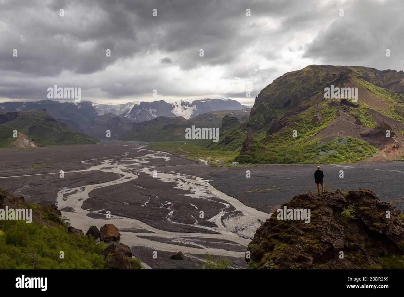 Escursionista femminile in piedi su uno sperone roccioso che guarda su Þórsmörk alla fine dell'escursione a Fimmvörðuháls in Islanda Foto Stock