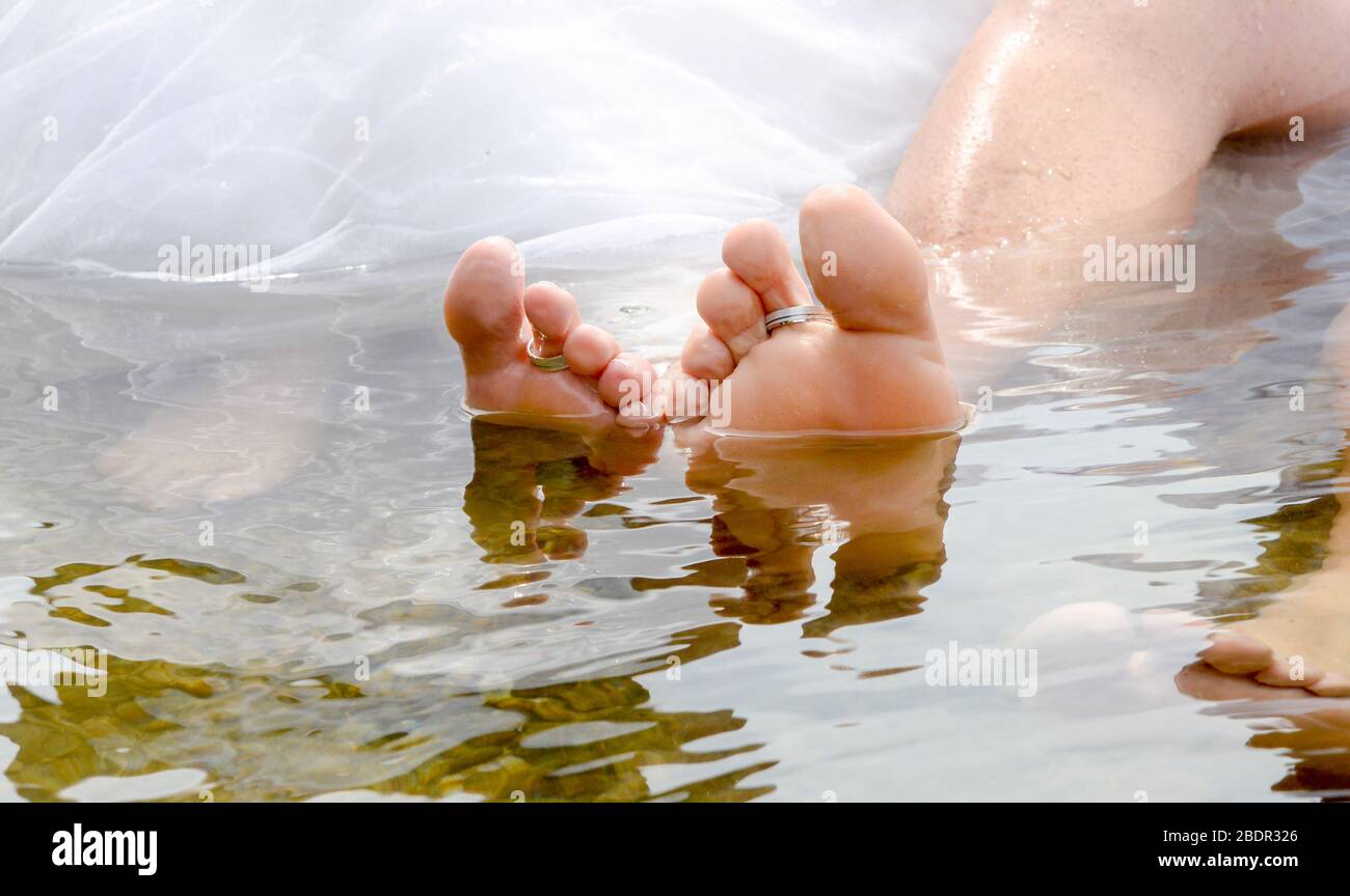 Anelli posti sui piedi sommersi nell'acqua degli sposi novelli. Foto Stock