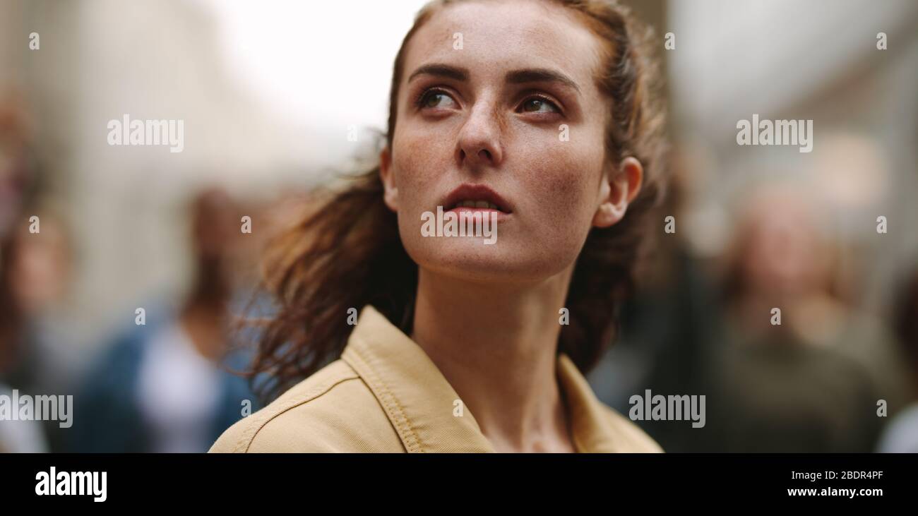 Primo piano dell'attivista femminile che guarda lontano con un gruppo di manifestanti sullo sfondo. Attivista femminile in mostra in città. Foto Stock Primo piano dell'attivista femminile che guarda lontano con un gruppo di manifestanti sullo sfondo. Attivista femminile in mostra in città. Foto Stock