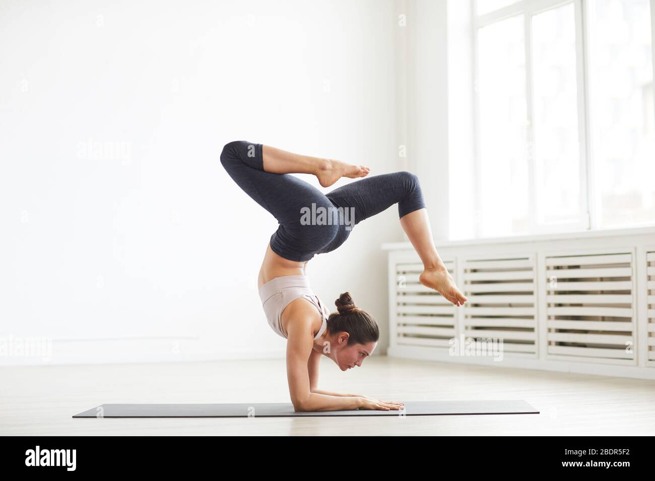 Giovane donna flessibile che fa esercizi sportivi sul tappetino per l'esercizio fisico in classe Foto Stock