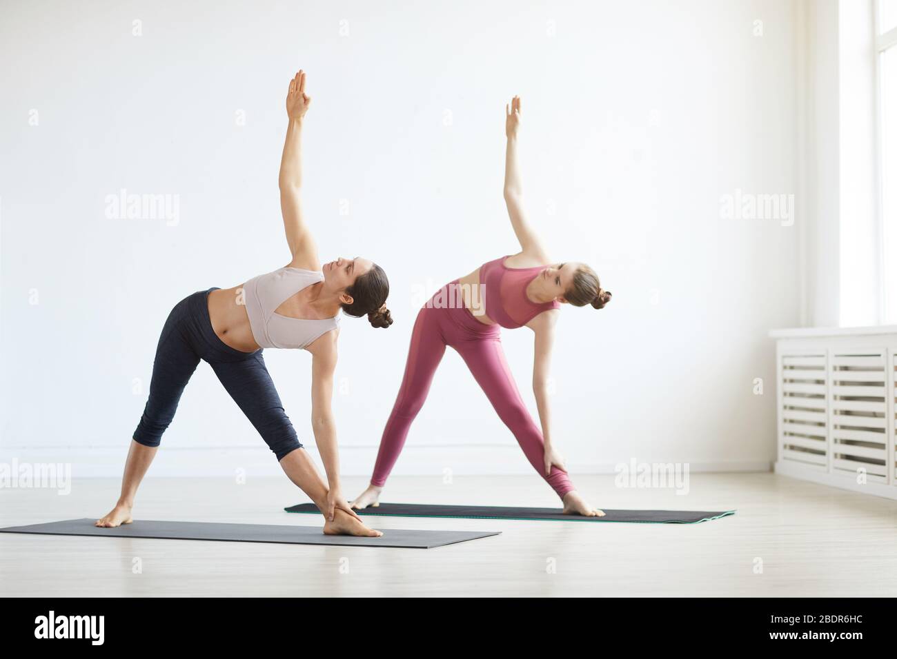 Due donne sane che allungano le mani mentre fanno le esercitazioni sul tappeto di esercitazione durante l'addestramento di sport Foto Stock