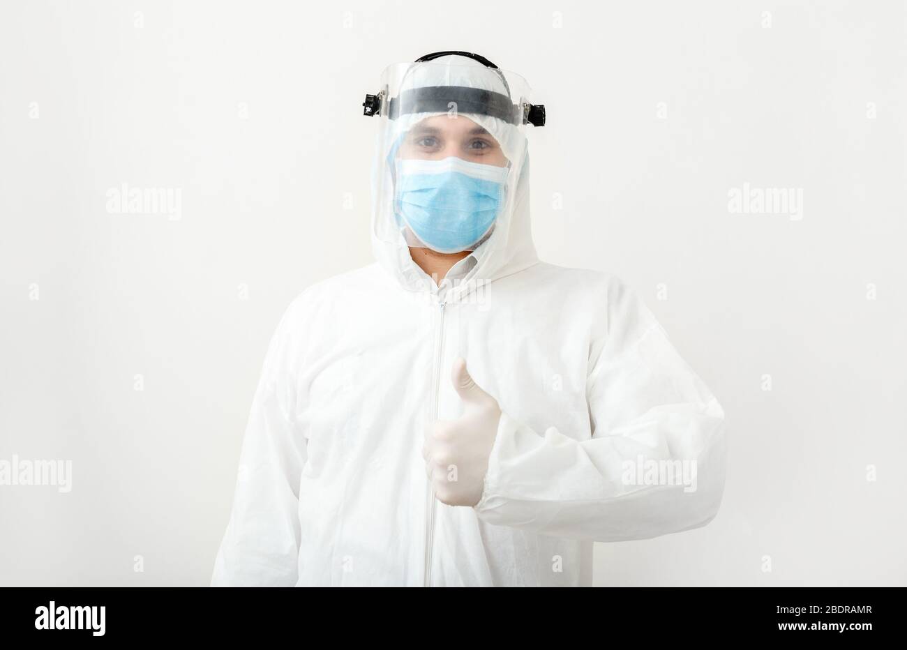 Disinfettante o medico che indossa tuta di protezione e maschera facciale con pollici rivolti verso l'alto, gesto positivo. Come alla fine della pandemia epidemia Covid-19 Foto Stock