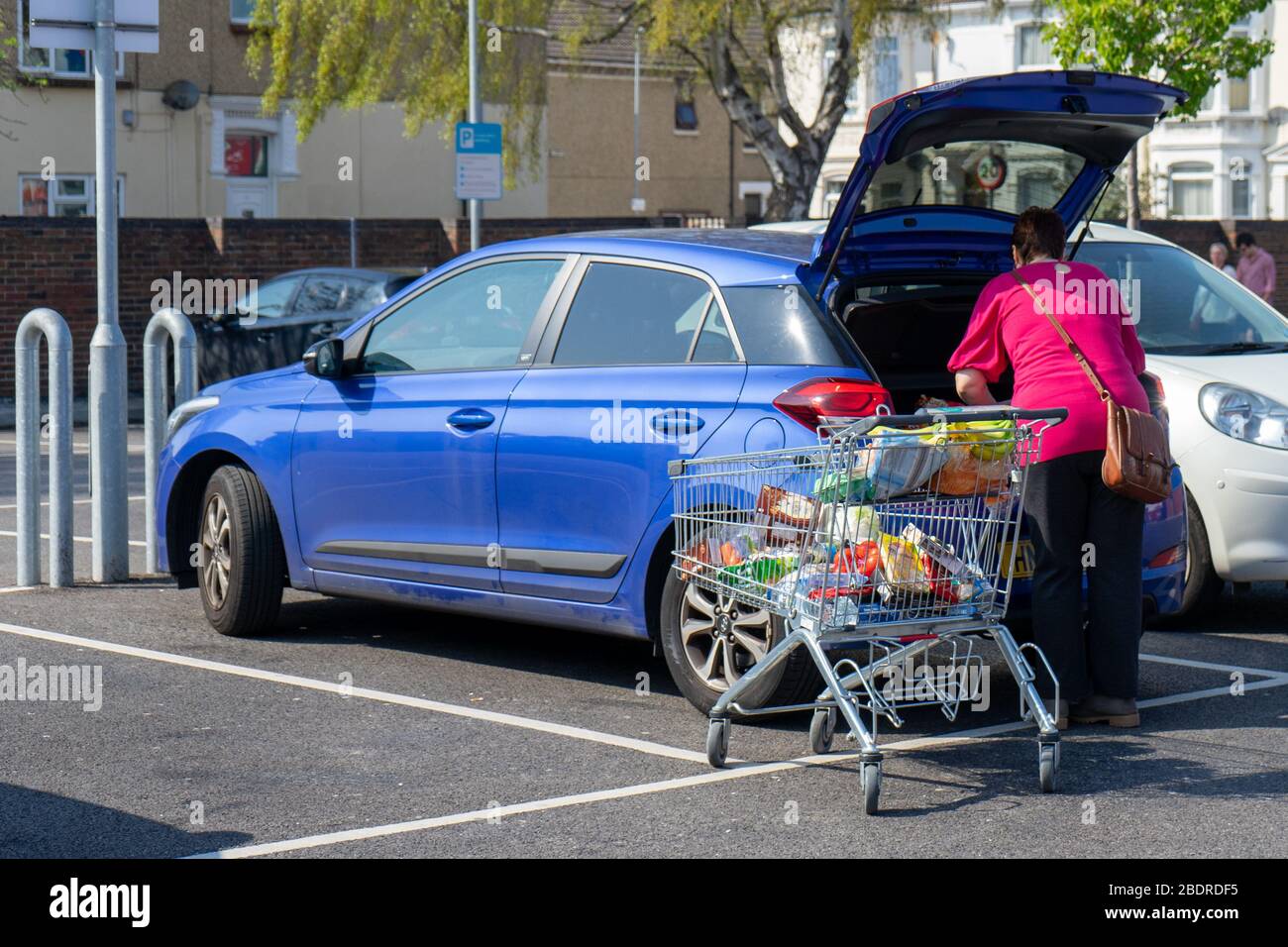 Una donna di mezza età che scarica il suo carrello pieno di shopping nel bagagliaio della sua auto o del suo tronco Foto Stock