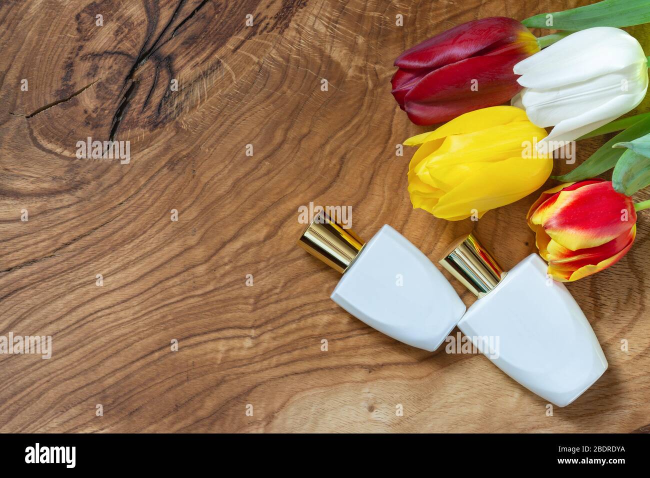 Due bottiglie di profumo bianco e un bouquet di tulipani multicolore su un asse naturale. Spazio di copia Foto Stock