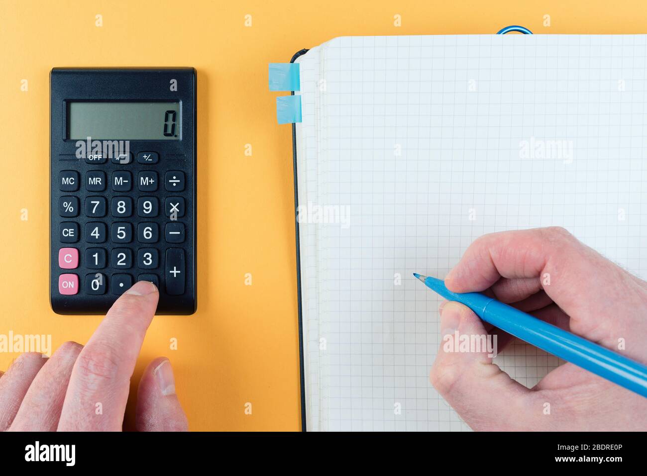 primo piano di persona utilizzando la calcolatrice tascabile mentre si prendono appunti sul blocco note su sfondo arancione Foto Stock