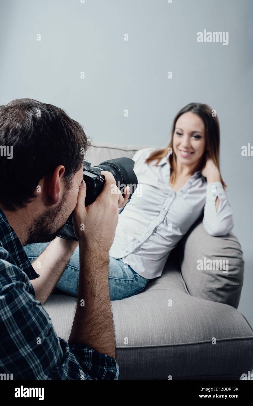 Professional photo shoot presso lo studio, un modello femminile è in posa su una poltrona e sorridente; il fotografo sta scattando alcune foto con il suo venuto digitale Foto Stock