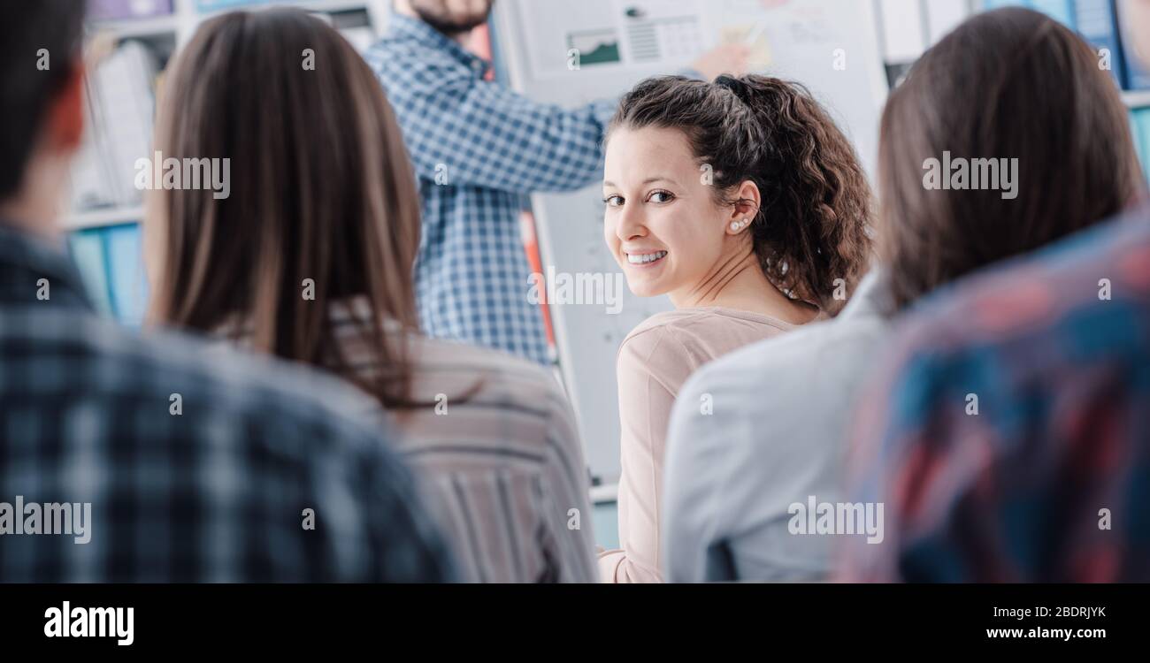 Uomo che presenta il suo progetto di business su una lavagna a un pubblico giovane, una donna guarda la macchina fotografica e sorridente Foto Stock