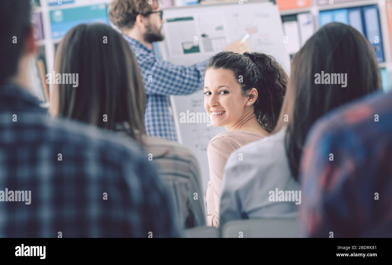 Uomo che presenta il suo progetto di business su una lavagna a un pubblico giovane, una donna guarda la macchina fotografica e sorridente Foto Stock