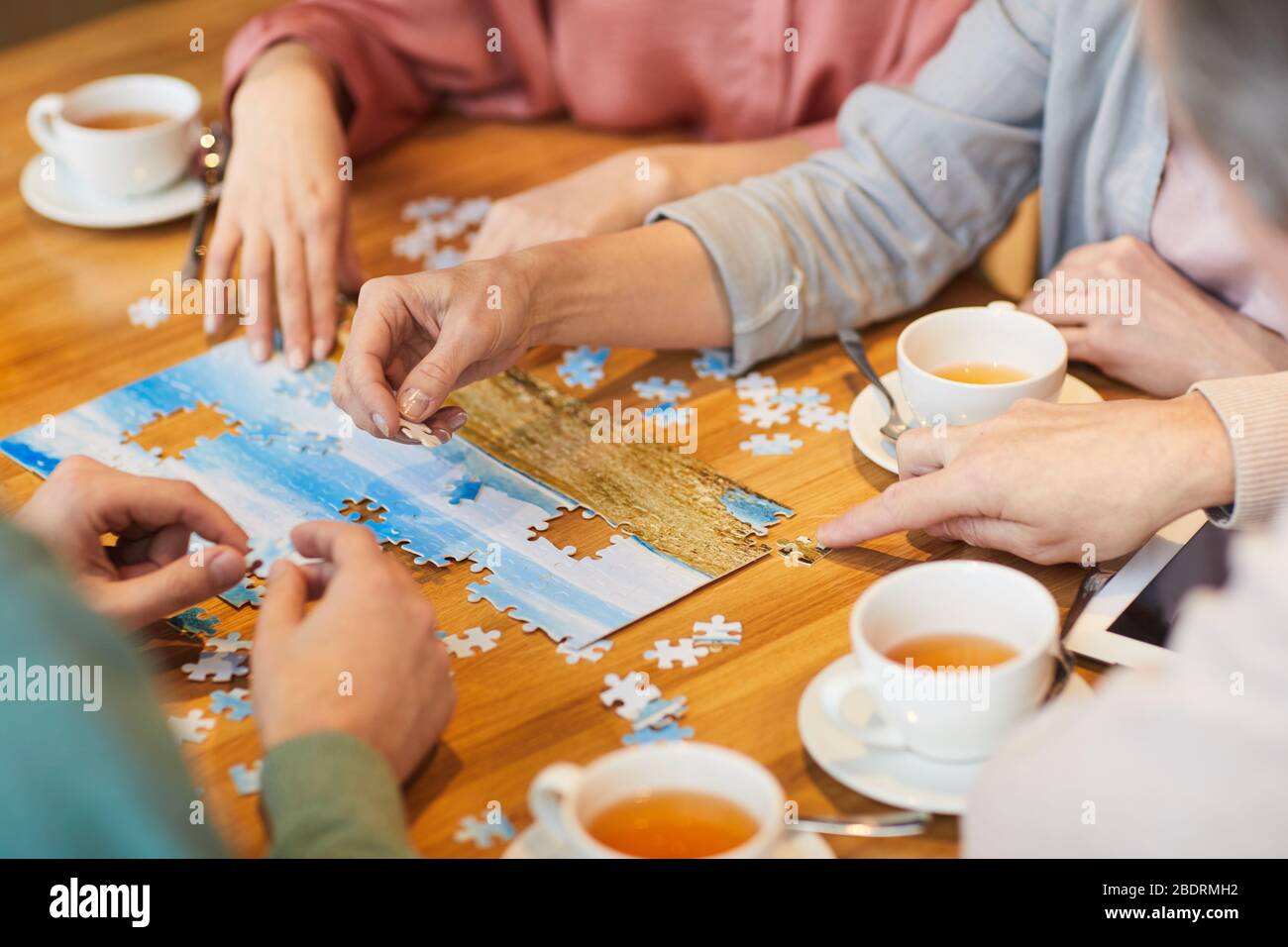 Primo piano di famiglia di quattro seduti al tavolo bere tè e raccogliere puzzle insieme Foto Stock