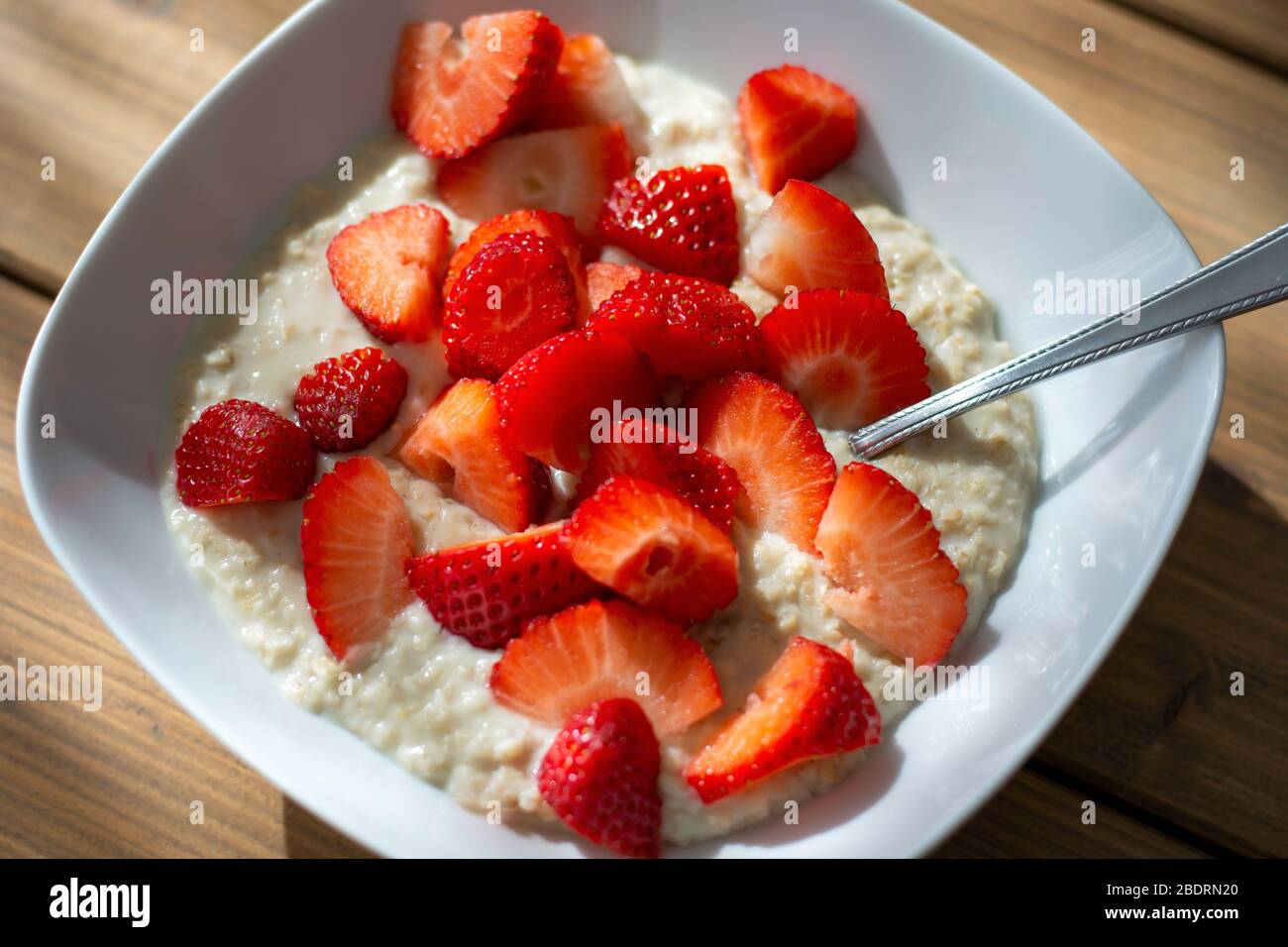 Vista dall'alto. Ciotola di porridge d'avena fatta in casa con fragole a fette sul tavolo alla luce del sole del mattino. Pasto sano. Porridge avena Foto Stock