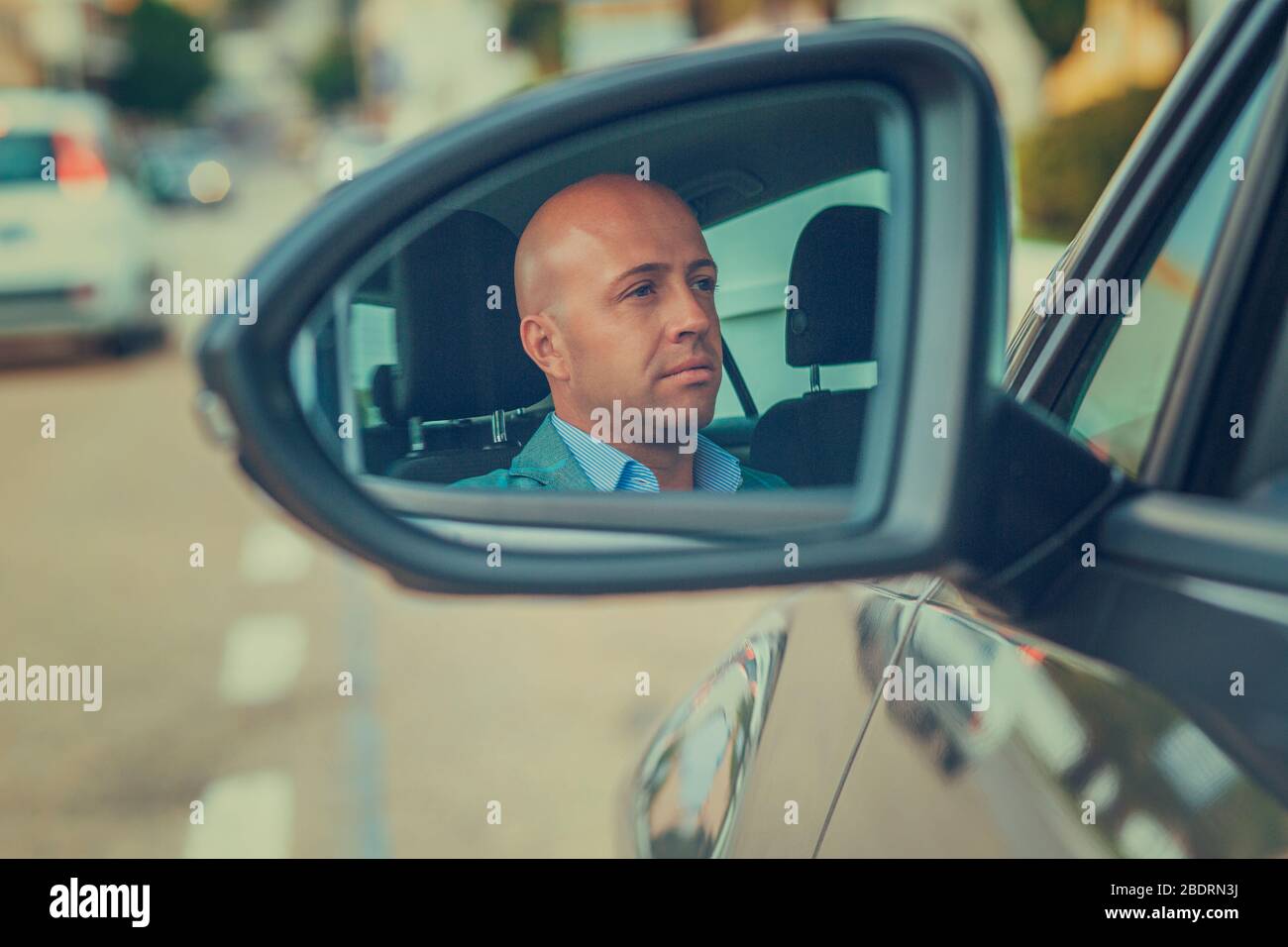 Un giovane uomo d'affari, un bel pilota sicuro nella sua auto che guarda al riflesso dello specchietto retrovisore esterno. Emozioni positive di espressione del volto umano. Sicuro Foto Stock