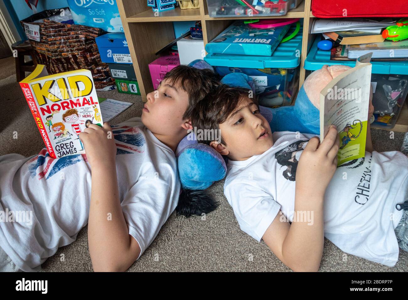 I giovani fratelli si trovano sul pavimento leggendo i loro libri. Ciò è durante la pandemia di coronavirus e la lettura id una buona attività educativa. Foto Stock