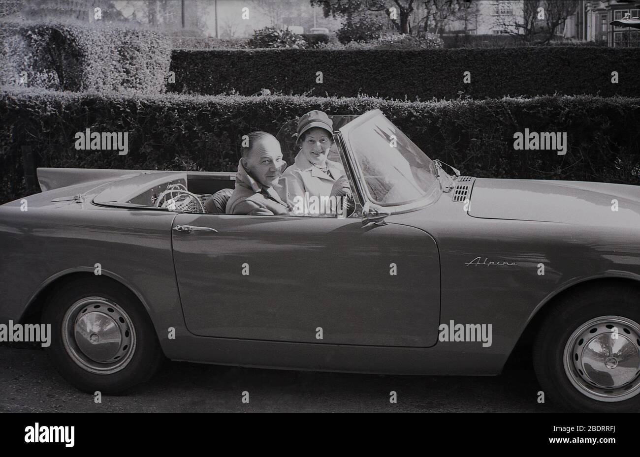 Anni '60, storico, in questo periodo, una coppia di mezza età seduto nella loro Sunbeam Alpine sport auto parcheggiato su un viale a Eastholm Green, Letchworth Garden City, Herts, Inghilterra, Regno Unito. Realizzata dal Gruppo Rootes, la produzione ha avuto una durata di 1953-1975, con la vettura vista dalla Serie i-IV dal 1959 al 1968. Foto Stock