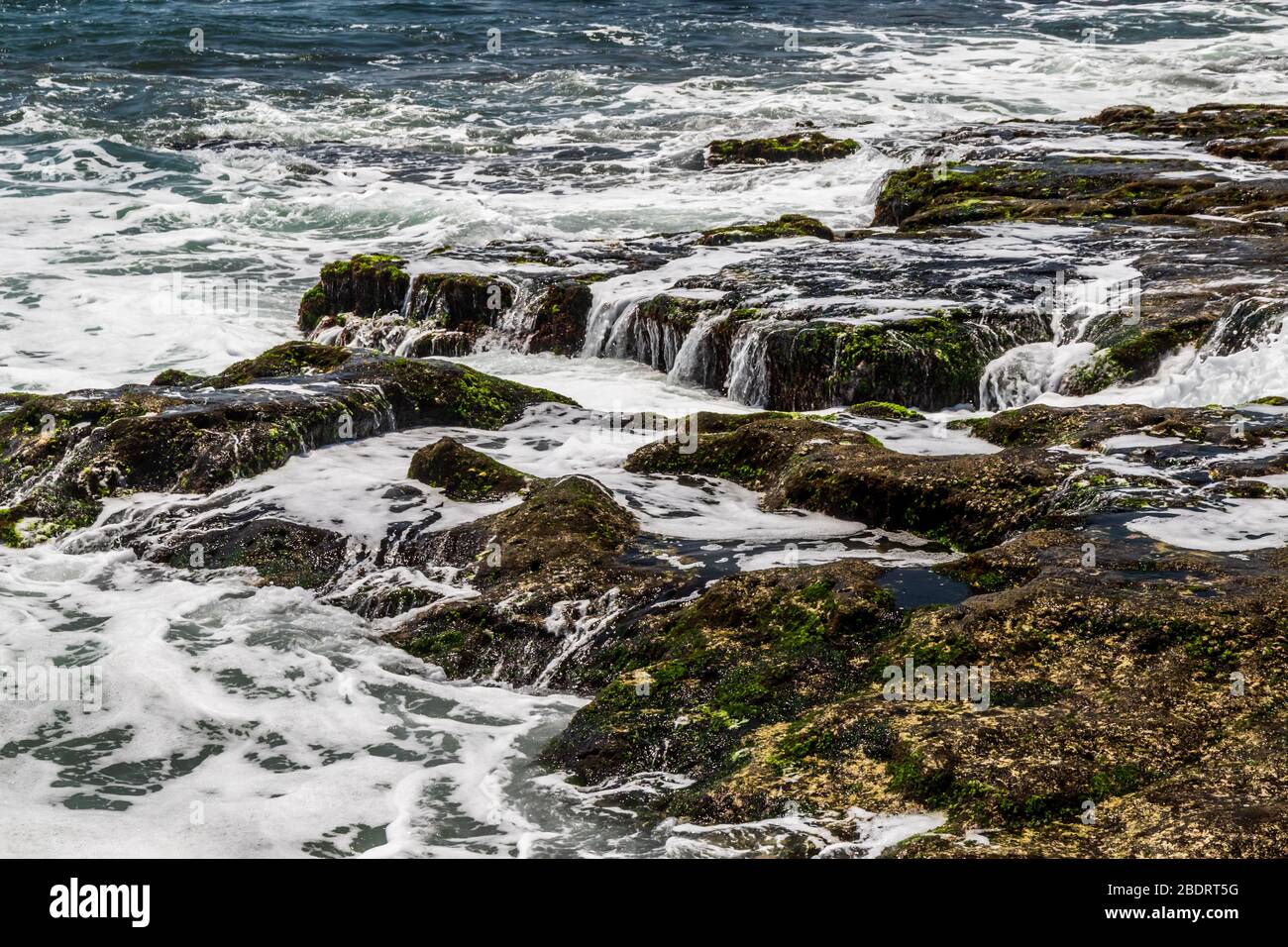 Acqua dell'oceano che scorre sulle rocce esposte alla bassa marea; Bali, Indonesia. Foto Stock