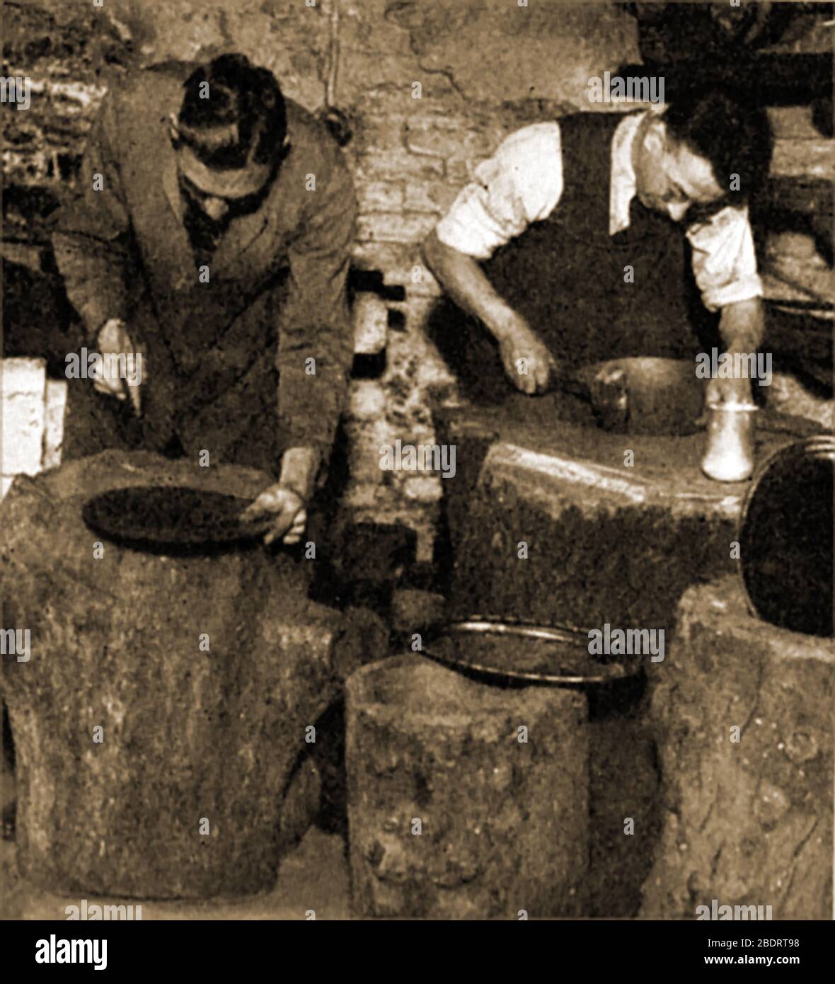 Una fotografia storica che mostra i lavoratori britannici peltro che battono le piastre in forma su tronchi di albero reali. Pewter è una delle più antiche industrie manifatturiere del Regno Unito in continua produzione. Il mestiere fu portato in Gran Bretagna dai Romani nel secondo secolo d.C. e fu introdotto a Sheffield nel 1769 da James Vickers che concepì una lega che potesse imitare il piatto d'argento. Negli anni '40 l'industria dei peltro impiegava centinaia di persone locali e. Foto Stock