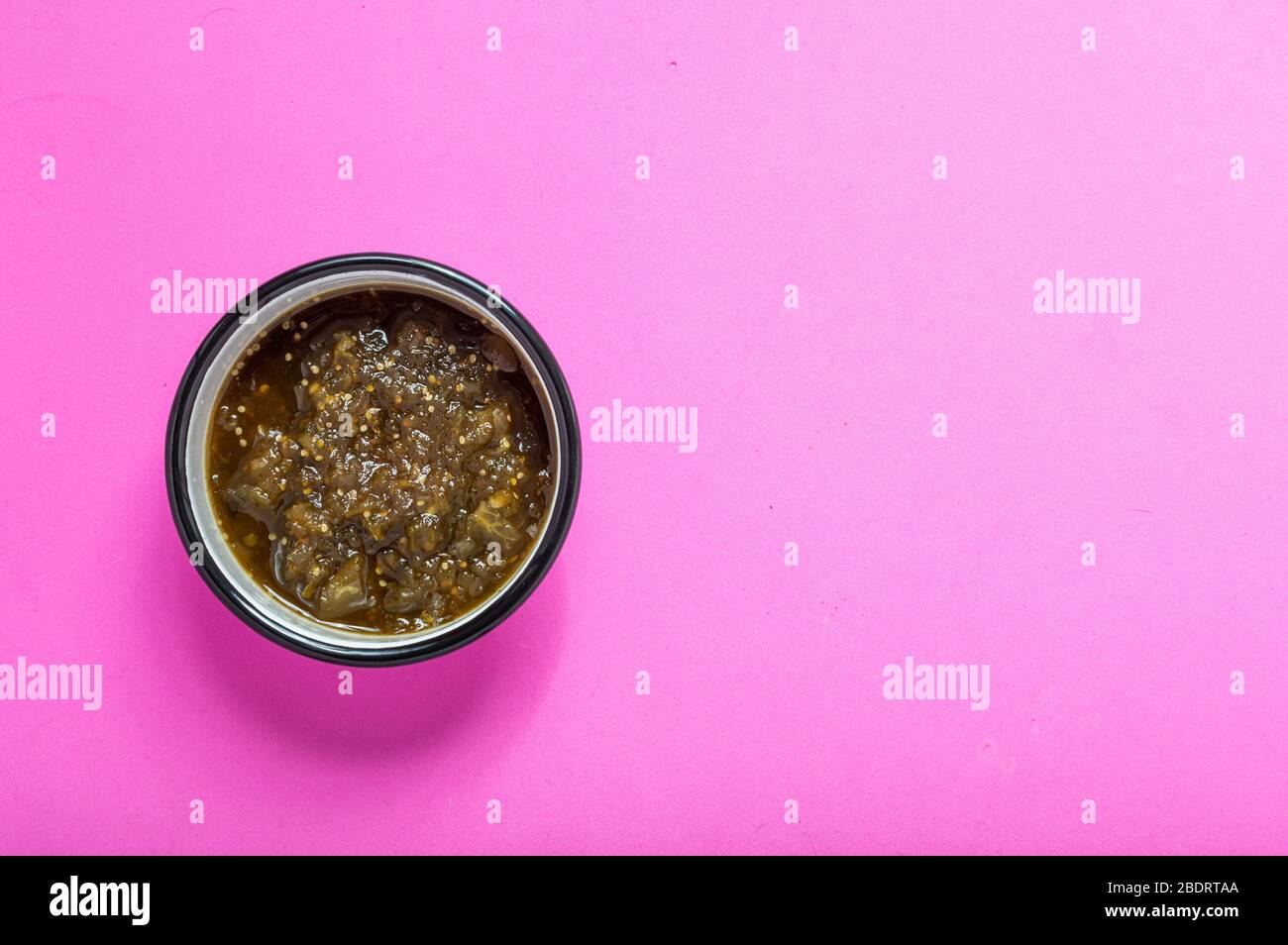 Salsa verde cotta su ciotola di smalto isolata su fondo rosa. Cibo messicano, condimenti. Foto Stock