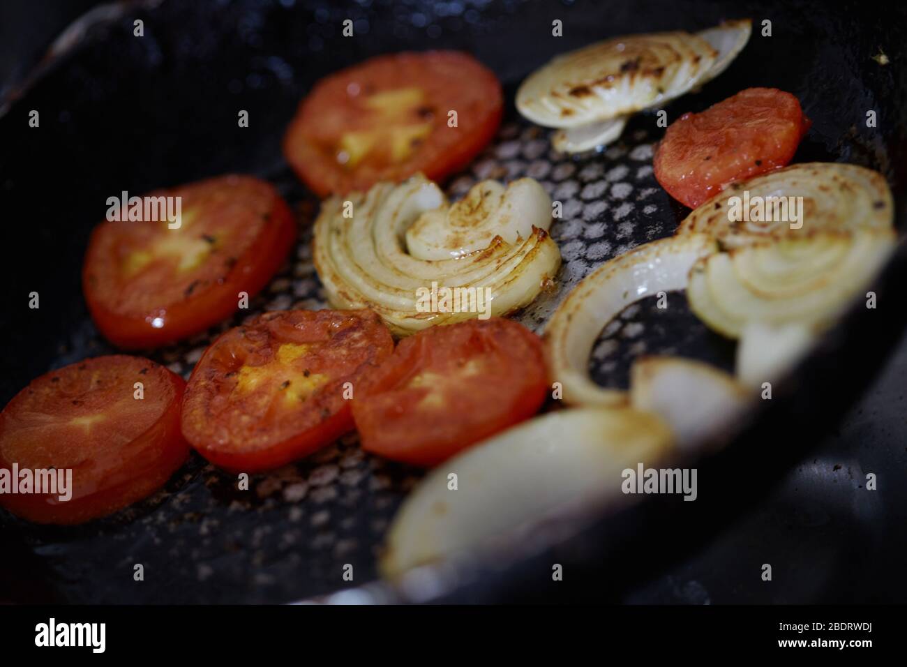 pomodori e cipolle fritti in una padella. Foto Stock