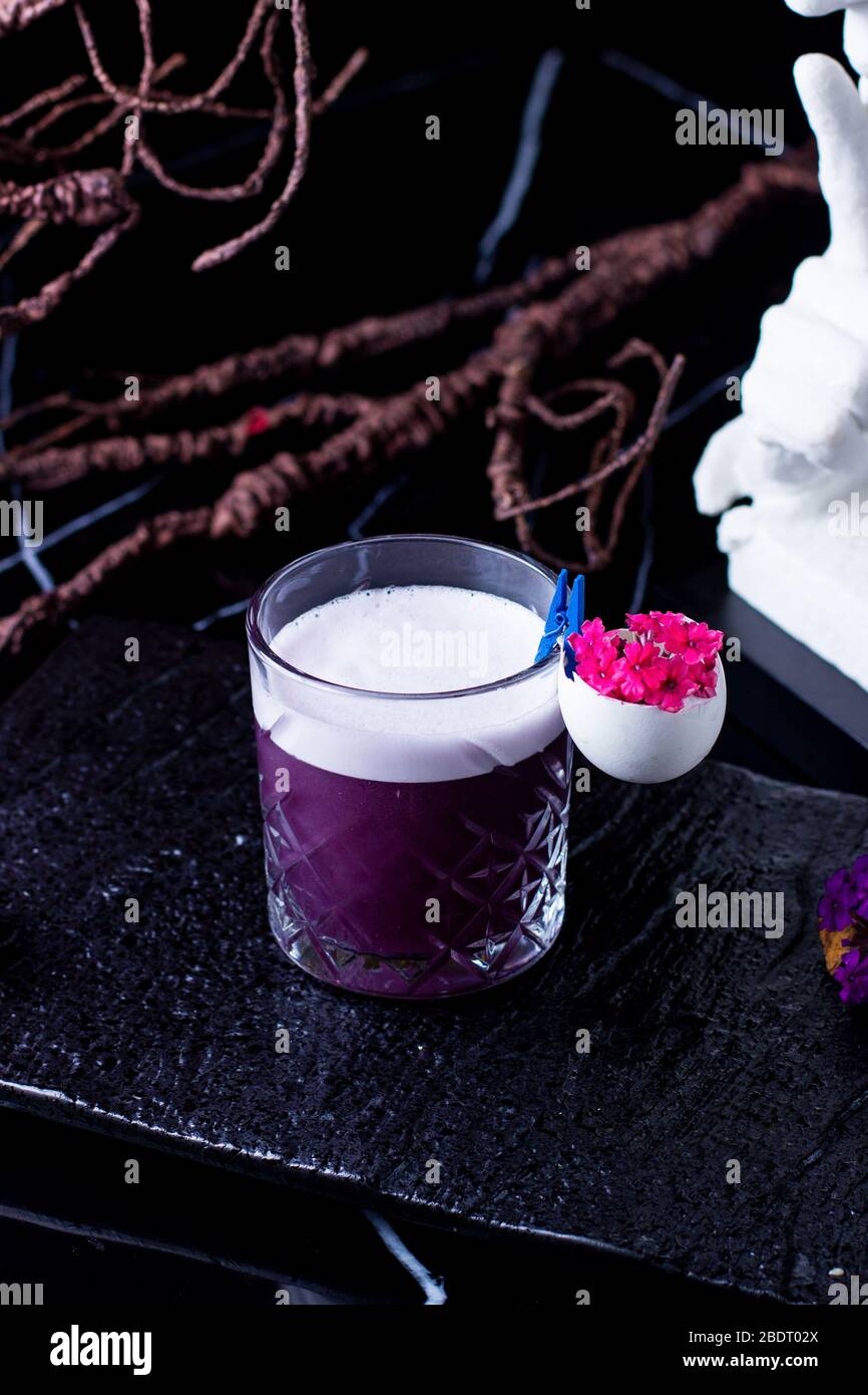 un bicchiere di cristallo di cocktail viola guarnito con fiore in guscio d'uovo Foto Stock