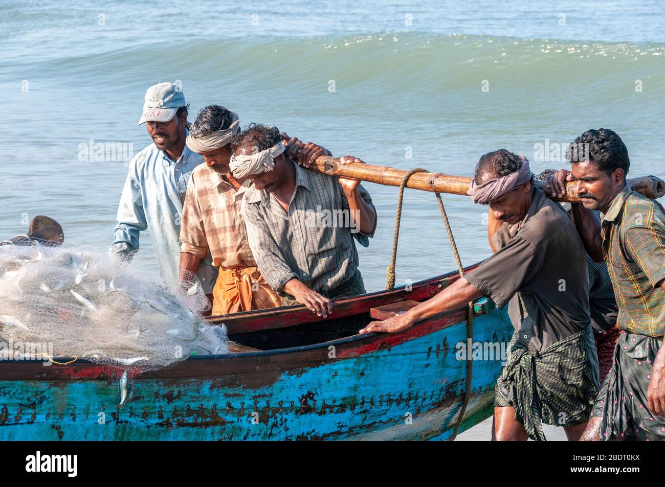 I pescatori che trasportano la loro tradizionale barca di legno dal mare sulla spiaggia di Marari dopo una gita di pesca di mattina presto. Kerala, India Foto Stock