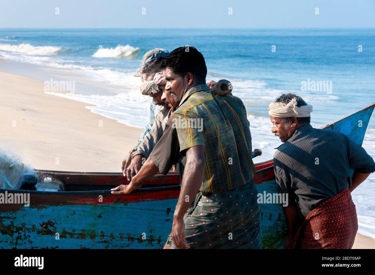 I pescatori che trasportano la loro tradizionale barca di legno dal mare sulla spiaggia di Marari dopo una gita di pesca di mattina presto. Kerala, India Foto Stock