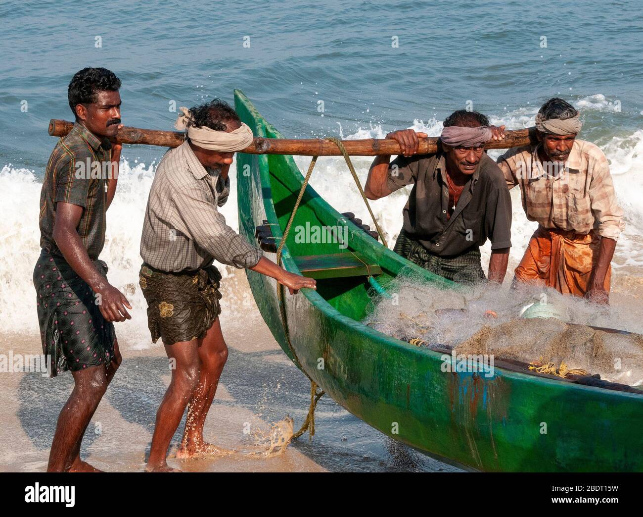 I pescatori che trasportano la loro tradizionale barca di legno dal mare sulla spiaggia di Marari dopo una gita di pesca di mattina presto. Kerala, India Foto Stock