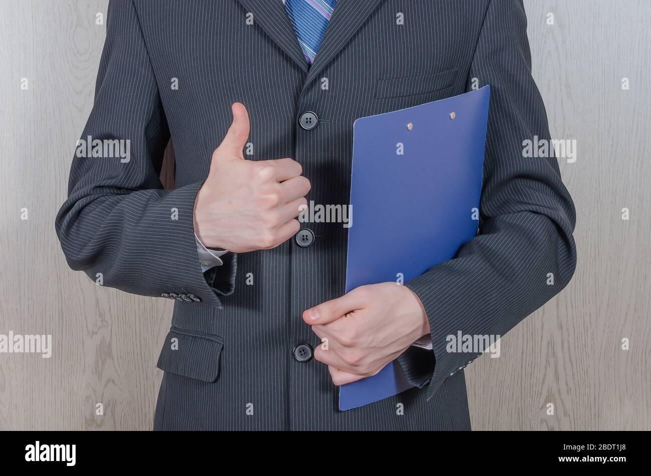 Un giovane in un vestito nero con una cartella mostra un gesto - tutto va bene. Proposta commerciale, partnership. Foto Stock