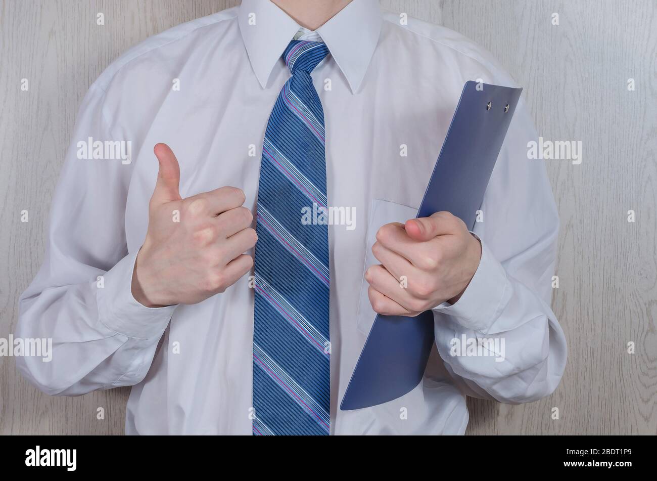 Un giovane uomo in una camicia bianca e cravatta con una piegatrice mostra un gesto - tutto va bene. Concetto aziendale. Proposta commerciale, partnership. Foto Stock